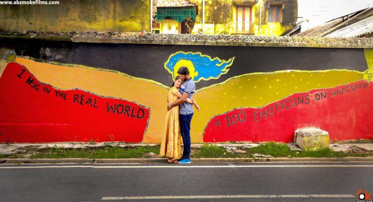 Couple hugging each other with a fancy painted wall behind