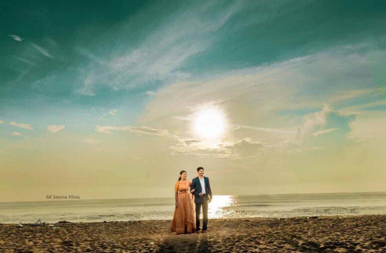 Couple holding each other arms and facing on the right side from the camera on a beach with a sun raising right behind them