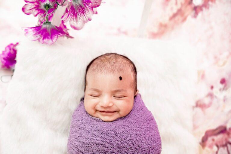 new born smiling wide inside a purple wrap with white fur and purple flowers on side