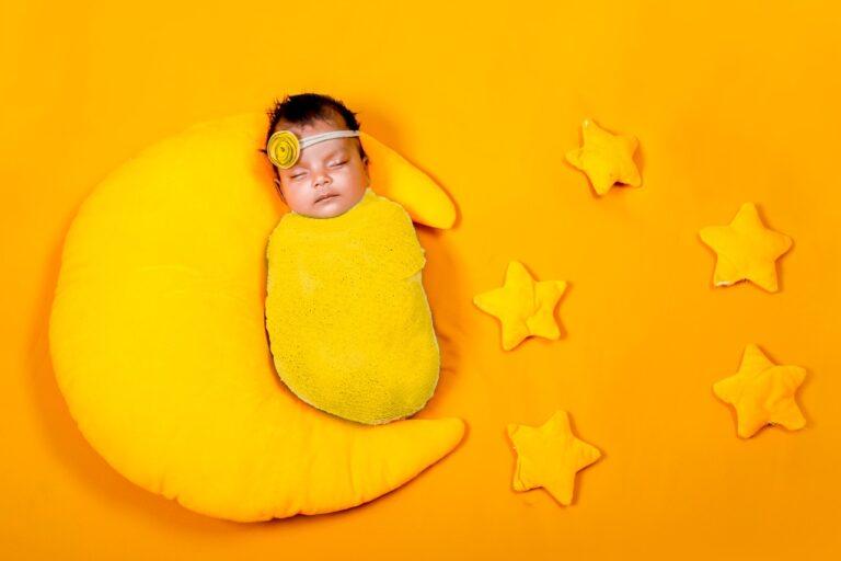 New born wrapped in a yellow wrap cloth lying on the half moon yellow pillows with the yellow stars on sides