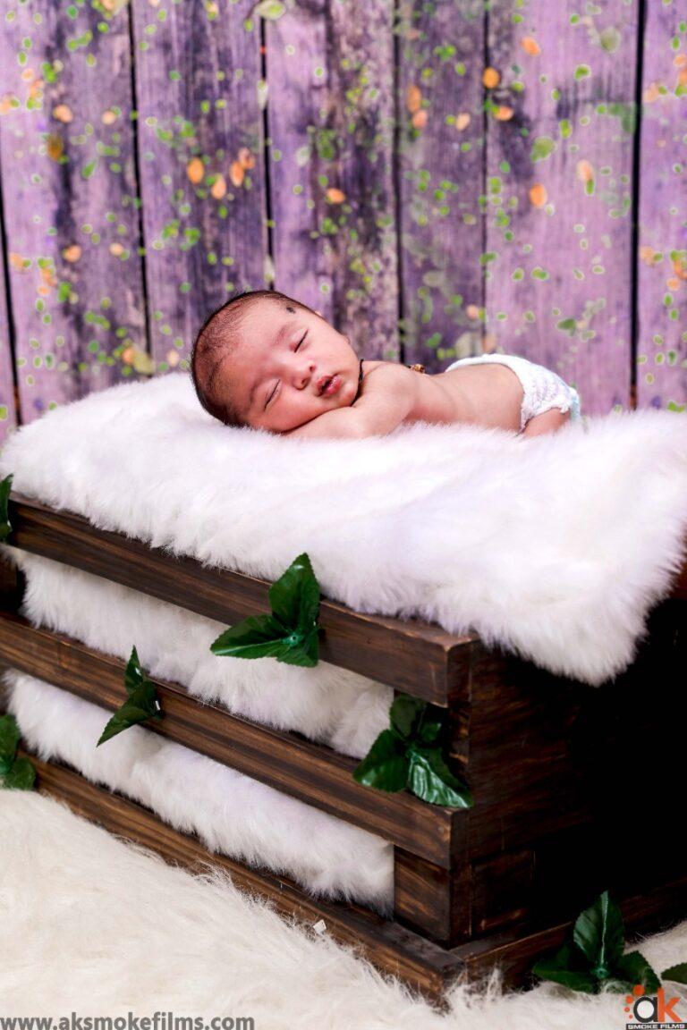 New born baby on tummy on a white fur filled wooden basket with green paper leaves there and here