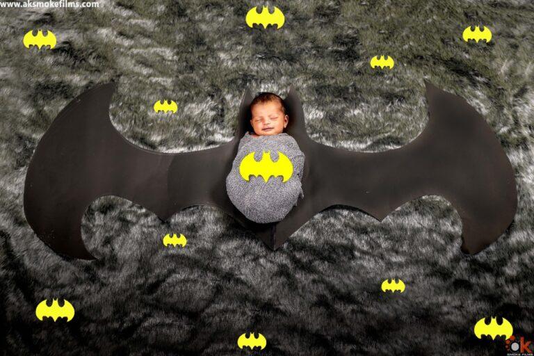 Newborn Baby smiling with the closed eyes in a batman wrap with the batman wing and black fur background