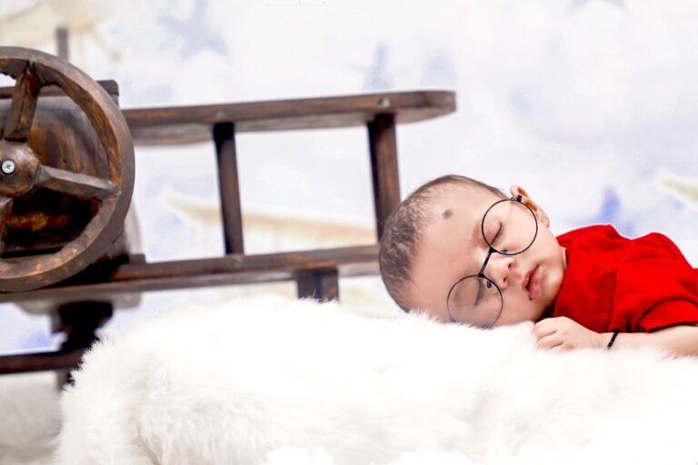 New born sleeping on his tummy with round specs with a wooden flight in the background