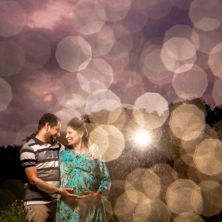 An expecting couple holding mother's tummy with a blur image of water droplets