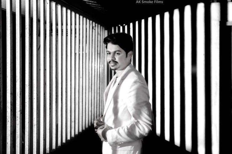 Groom in black and white with a background of set of rods with reflection of lights on the wall