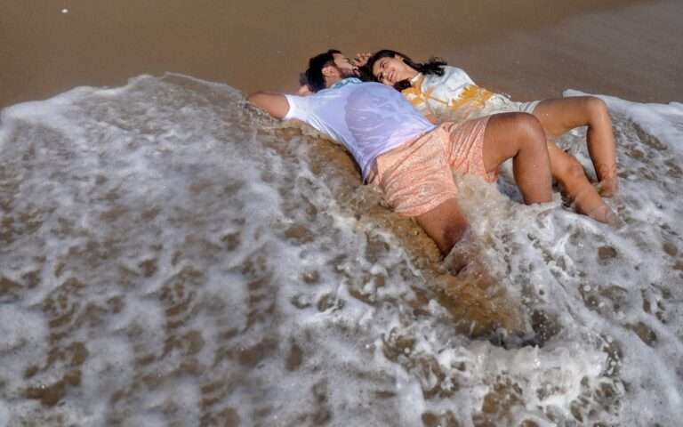 groom bride lying on the seashore when waves approaching them facing each other