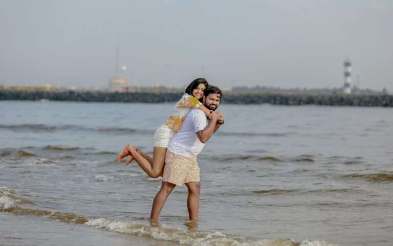 Groom holding bride from the back and lifting her in a seashore looking at the camera
